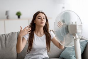 Mulher sentindo calor dentro de casa com uso de ventilador.